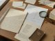 Oblique-angle documentary photo of an archival workbench: glass weights holding fragile poem pages with